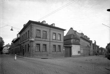 Das Foto zeigt das Gebäude des "Kaiserhofs", ein großes, zweistöckiges Backsteinhaus an einer Straßenecke. Weitere Gebäude reihen sich entlang der Straße, darunter eines mit dem Schriftzug "Peter Boller".