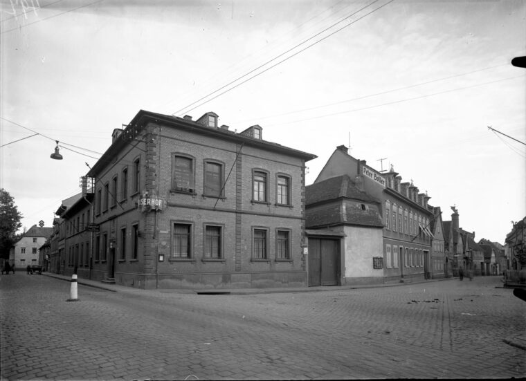 Das Foto zeigt das Gebäude des "Kaiserhofs", ein großes, zweistöckiges Backsteinhaus an einer Straßenecke. Weitere Gebäude reihen sich entlang der Straße, darunter eines mit dem Schriftzug "Peter Boller".