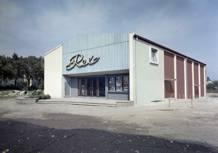 Ein farbiges Foto zeigt das Hochheimer Kino "Rex" mit einem großen, geschwungenen Schriftzug des Namens über dem Eingang. Das Gebäude hat eine hellblaue Fassade.