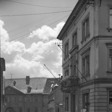 Das Schwarz-Weiß-Foto zeigt das alte Rathaus in der Kirchstraße 13 in Hochheim am Main. Das Gebäude hat einen Balkon und dominiert die rechte Seite des Bildes, während die Kopfsteinpflasterstraße und weitere Gebäude im Hintergrund zu sehen sind.