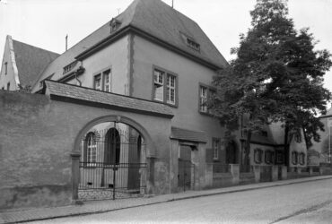 Das Foto zeigt die Außenansicht des Gebäudes vom Hochheimer Amtsgericht. Das Gebäude ist von einem Baum und weiteren alten Häusern umgeben.