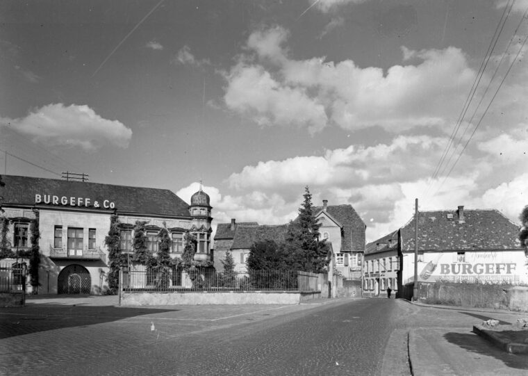 Das Foto zeigt ein Gebäude der Sektkellerei "Burgeff & Co." mit einem markanten Turm und zahlreichen Fenstern. Die Straße im Vordergrund ist gepflastert. Rechts ist eine große Werbetafel der Sektkellerei zu erkennen.