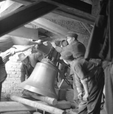 Eine Gruppe von Männern arbeitet zusammen, um eine große Glocke in einem Glockenturm zu befestigen.