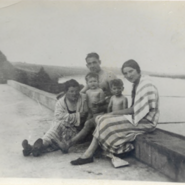 Eine Familie sitzt auf der Terrasse über den Umkleideräumen des Strandbads. Im Hintergrund ist das Mainufer in Hochheim zu sehen. Die Szene vermittelt eine entspannte, sommerliche Stimmung.